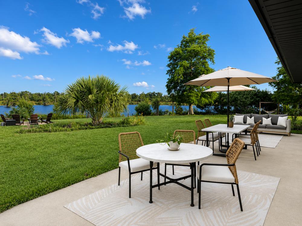 Round dining table and lounge seating on the patio, lake and lawn beyond